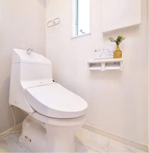 白を基調とした清潔感のあるトイレ空間で、壁に小さな観葉植物が飾られている