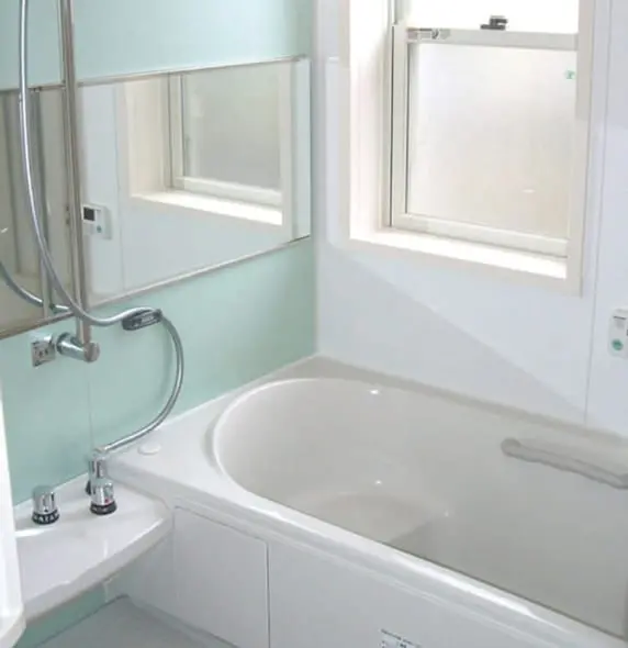 白と淡いグリーンを基調とした清潔感のある浴室で、大きな鏡と窓が特徴的